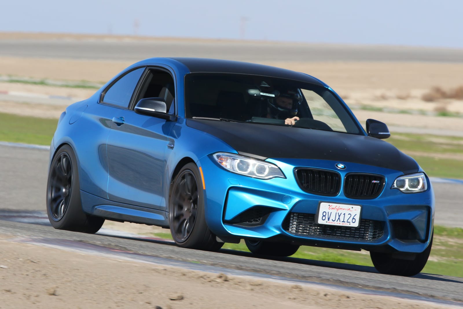 A blue BMW M2 cornering on track at Buttonwillow Raceway Park.