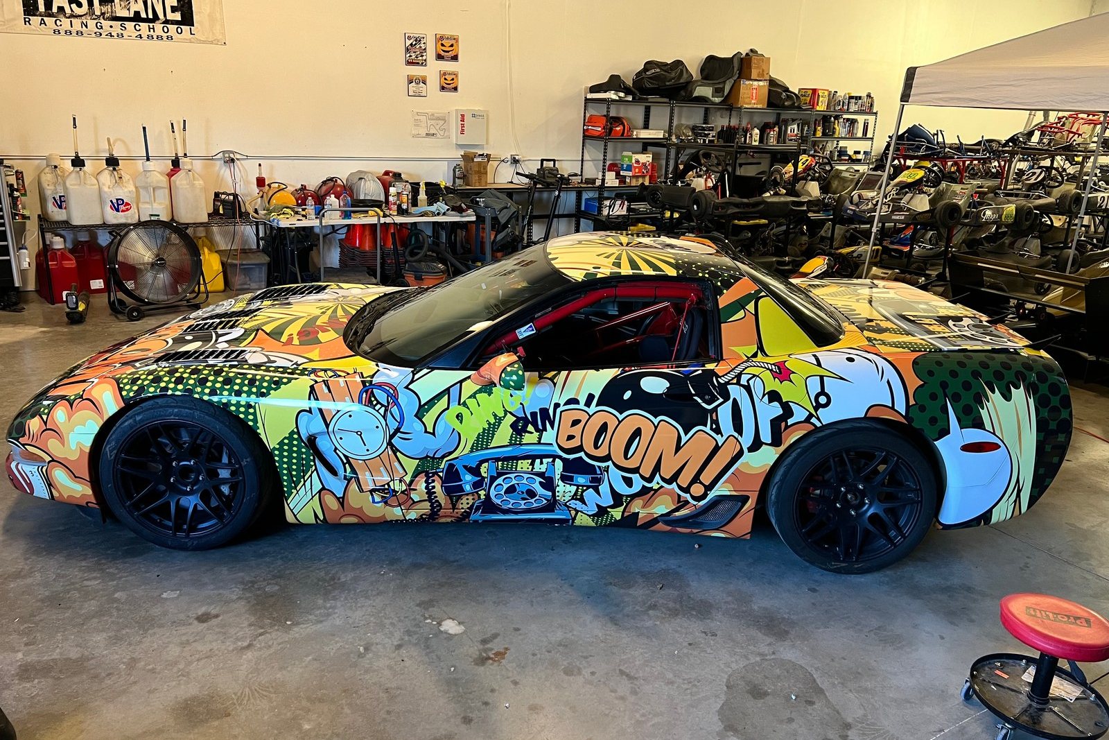 A FastLane Spec Corvette in a comic-art wrap in the FastLane shop at Buttonwillow.