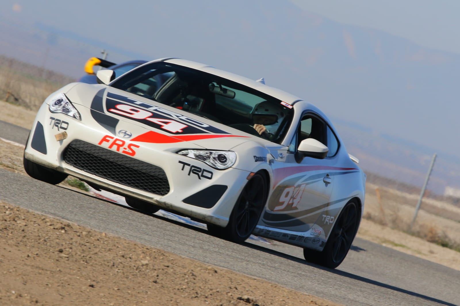 A white FastLane Toyota GR86 / FRS in TRD livery cornering on track at Buttonwillow Raceway.