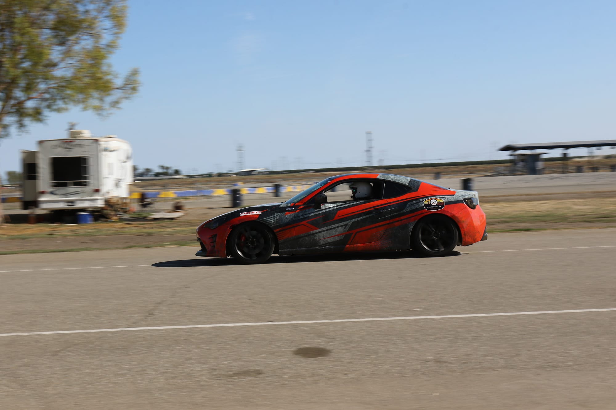 A liveried sports car at speed on the circuit at Buttonwillow Raceway Park.