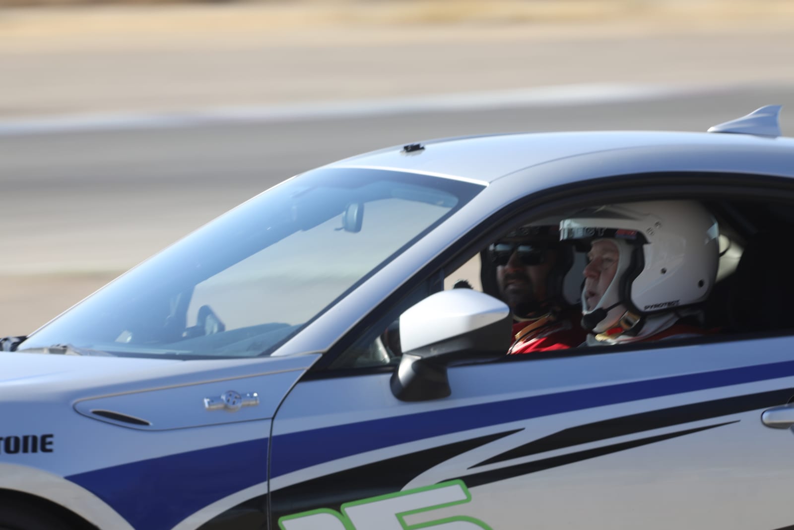 A FastLane instructor coaching a student driver trackside at Buttonwillow.