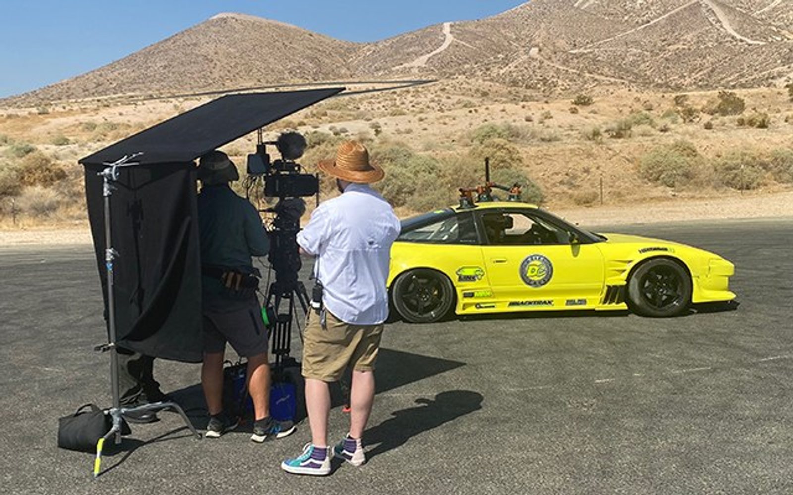 A film crew with a cinema camera shooting a FastLane picture car on track at Buttonwillow.